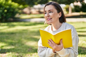 Fototapeta premium Middle age woman reading book sitting on herb at park