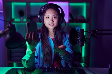 Young asian woman playing video games with smartphone smiling cheerful offering palm hand giving assistance and acceptance.