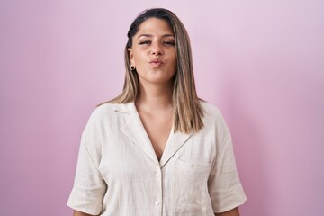 Obraz premium Blonde woman standing over pink background looking at the camera blowing a kiss on air being lovely and sexy. love expression.