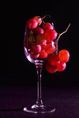 Broken glass with delicious grapes on table against dark background