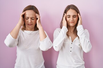 Middle age mother and young daughter standing over pink background with hand on head, headache...