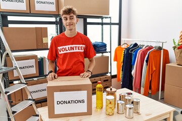 Young caucasian man volunteer holding donations box smiling looking to the side and staring away...