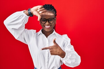 African woman with braids standing over red background smiling making frame with hands and fingers with happy face. creativity and photography concept. © Krakenimages.com