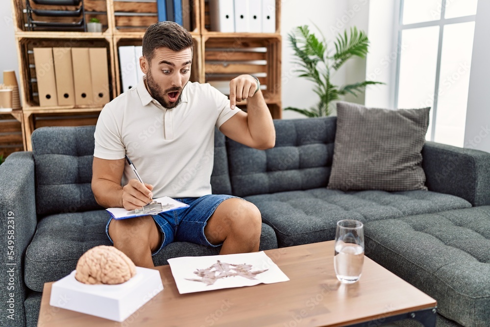 Canvas Prints handsome hispanic man working with rorschach test at psychology clinic pointing down with fingers sh