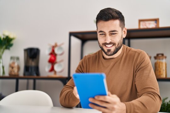 Young hispanic man using touchpad sitting on table at home