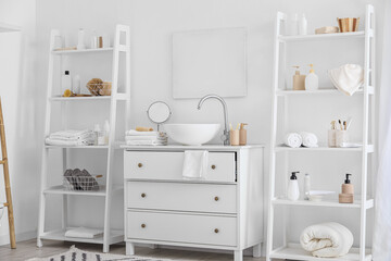 Fototapeta na wymiar Shelf units with bath accessories and modern sink near white wall in bathroom interior
