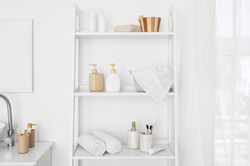 Fototapeta na wymiar Shelf unit with bath accessories near white wall in bathroom