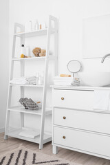 Fototapeta na wymiar Chest of drawers with modern sink and shelf unit with bath accessories near white wall