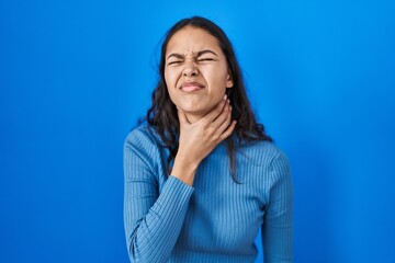 Young brazilian woman standing over blue isolated background touching painful neck, sore throat for...