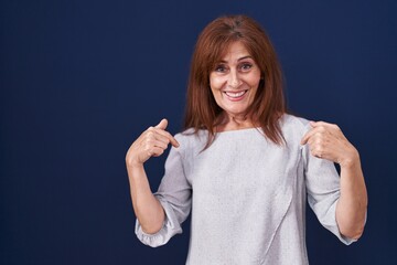 Fototapeta premium Middle age woman standing over blue background looking confident with smile on face, pointing oneself with fingers proud and happy.