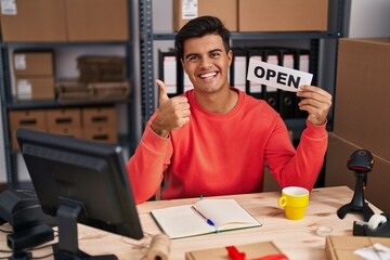 Hispanic man working at small business ecommerce holding open banner smiling happy and positive,...