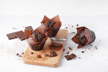 Wooden board with tasty chocolate muffins on light background