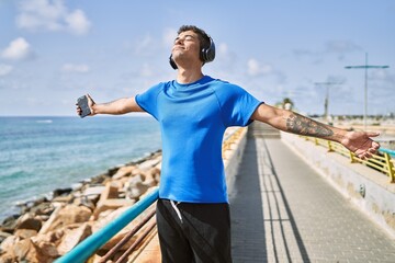 Young latin man breathing using headphones and smartphone at the beach.