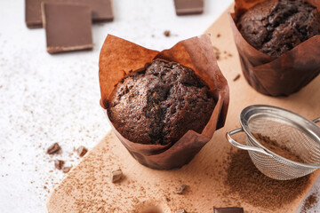 Wooden board with tasty chocolate muffins on light background, closeup