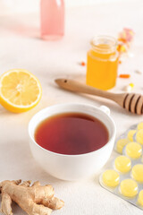 Cup of tea, pills for sore throat and ginger on white background, closeup