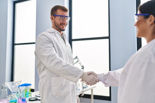 Man and woman scientist partners smiling confident shake hands at laboratory