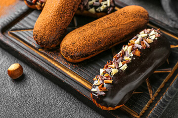 Wooden board with sweet chocolate eclairs on dark background, closeup
