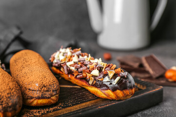 Wooden board with sweet chocolate eclairs on dark background, closeup