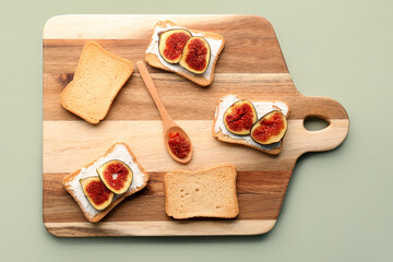 Wooden board of tasty bruschettas with cream cheese and figs on color background