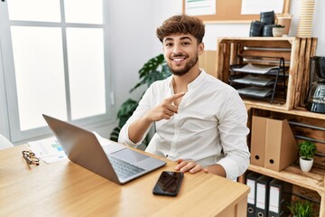Obraz premium Young arab man working using computer laptop at the office smiling happy pointing with hand and finger to the side
