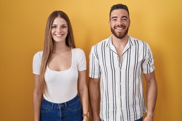 Young couple standing over yellow background with a happy and cool smile on face. lucky person.