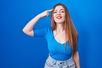 Redhead woman standing over blue background smiling pointing to head with one finger, great idea or thought, good memory