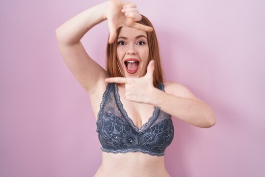 Redhead woman wearing lingerie over pink background smiling making frame with hands and fingers with happy face. creativity and photography concept.