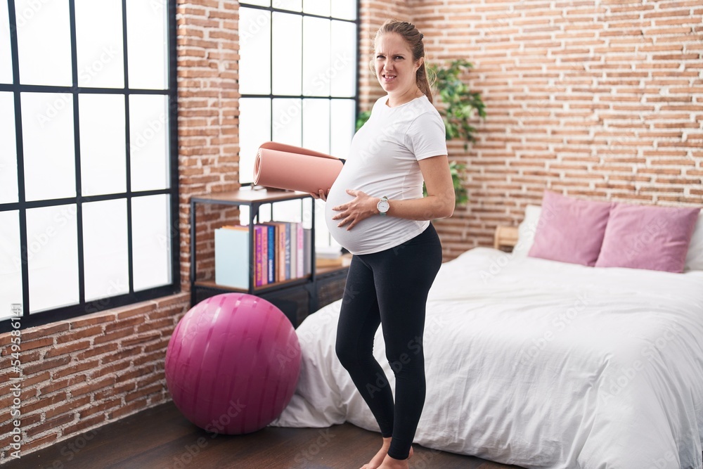 Poster young pregnant woman holding pilate mat at bedroom clueless and confused expression. doubt concept.