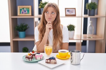 Obraz na płótnie Canvas Young caucasian woman eating pastries t for breakfast looking confident at the camera smiling with crossed arms and hand raised on chin. thinking positive.