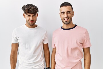 Young gay couple standing over isolated background winking looking at the camera with sexy expression, cheerful and happy face.