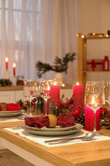 Christmas table setting with burning candles, fir cones and rowan in kitchen, closeup
