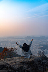 A woman who sits on a rock at the top of the mountain in front of Daegu and enjoys the autumn mood