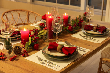 Christmas table setting with burning candles, fir cones and rowan in kitchen
