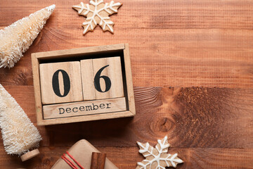 Cube calendar with date 6 DECEMBER, Christmas trees, cookies and gift on wooden background