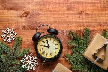 Alarm clock with Christmas branches, gift and snowflakes on wooden background