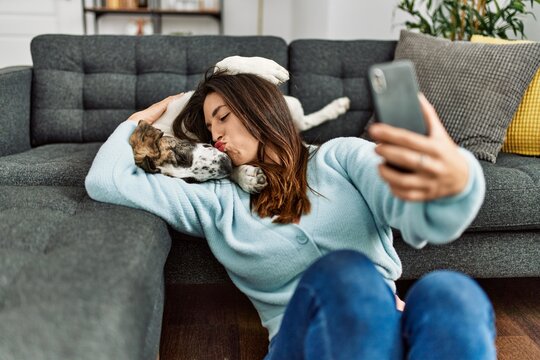 Young woman kissing and hugging dog making selfie by the smartphone at home