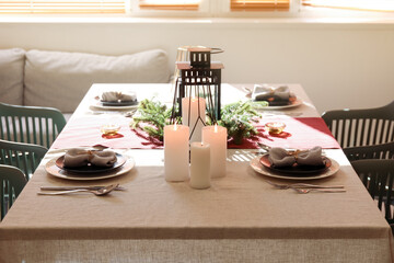 Christmas table setting with wreath and burning candles in dining room