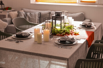 Christmas table setting with wreath and burning candles in dining room