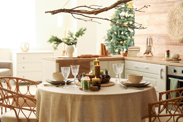 Christmas table setting with burning candles and wreath in kitchen