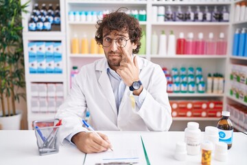 Hispanic young man working at pharmacy drugstore pointing to the eye watching you gesture,...
