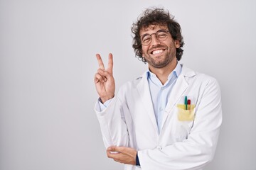 Hispanic young man wearing doctor uniform smiling with happy face winking at the camera doing...