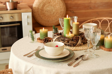 Christmas table setting with burning candles and wreath in kitchen