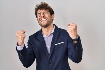 Hispanic business man wearing glasses very happy and excited doing winner gesture with arms raised, smiling and screaming for success. celebration concept.