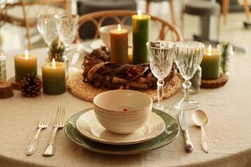 Fototapeta na wymiar Christmas table setting with burning candles and wreath in kitchen, closeup