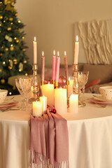 Christmas table setting with burning candles and balls in dining room