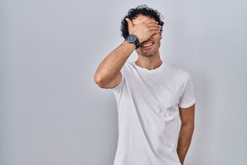 Hispanic man standing over isolated background smiling and laughing with hand on face covering eyes...