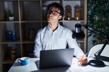 Obraz premium Hispanic man working at the office at night smiling looking to the side and staring away thinking.