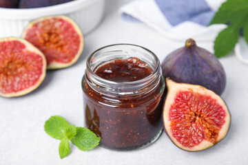 Fototapeta na wymiar Glass jar of tasty sweet fig jam and fruits on light table, closeup