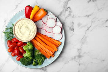Plate with delicious hummus and fresh vegetables on white marble table, top view