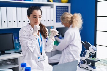 Young hispanic woman working at scientist laboratory serious face thinking about question with hand on chin, thoughtful about confusing idea